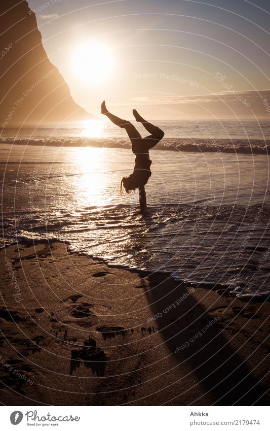 Junge Frau macht Handstand am Strand im Wasser im Gegenlicht am Abend Balance kopfüber Figur Yoga Meer Gesundheit Silhouette Ausgeglichenheit Lifestyle