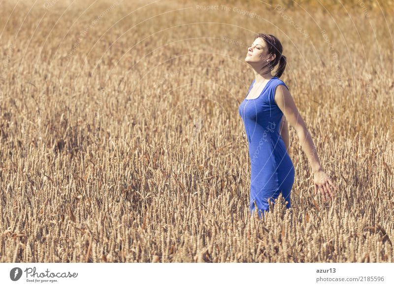 Schöne junge Frau im Herbst auf Getreide Feld bis zum Horizont. Hübsches Mädchen mit Lebensfreude geniesst die Sonnenschein Pause und das Leben. Erholung und Energie tanken vom Zeit Stress in der Umwelt und Natur Idylle. Blaues Kleid.