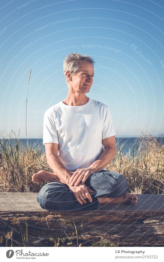 Mann, der in einer entspannten Yogahaltung am Strand sitzt. Erholung Meditation Sonne Erwachsene sitzen natürlich Kraft Gelassenheit 50-60 Jahre Aktion Farbbild