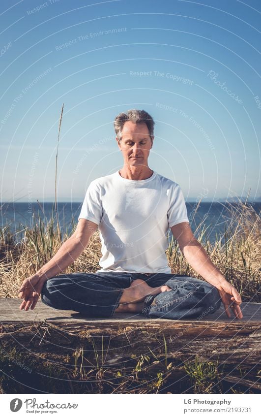 Mann, der in einer entspannten Yogahaltung am Strand sitzt. Erholung Meditation Sonne Erwachsene sitzen natürlich Kraft Gelassenheit 50-60 Jahre Aktion Farbbild