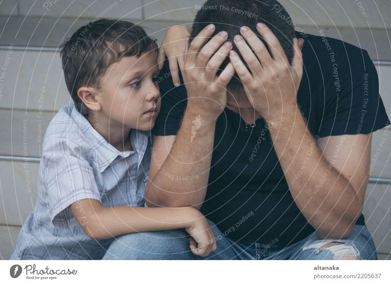 Porträt von jungen traurigen kleinen Jungen und Vater sitzen im Freien an der Tageszeit. Konzept der Traurigkeit. Gesicht Kind Mann Erwachsene Eltern