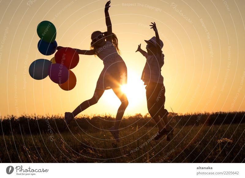 Silhouette von zwei glücklichen Kindern, die zur Zeit des Sonnenuntergangs auf dem Spielfeld spielen. Sie haben Spaß in der Natur. Lifestyle Freude Glück