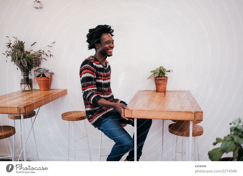 Junger glücklicher afroamerikanischer Mann, der im Café sitzt. Lifestyle Freude Erholung Tisch Restaurant Mensch Erwachsene Jugendliche Afro-Look Holz Lächeln
