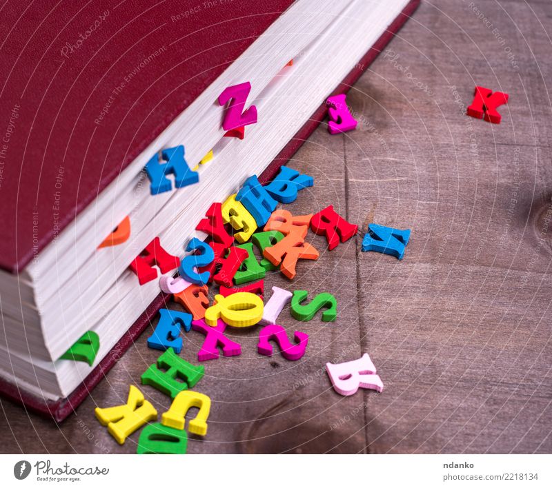 Holzbuchstaben fallen aus einem geschlossenen Buch Tisch lesen blau braun rosa rot Idee lernen Schule Brief Information farbenfroh zugeklappt Deckung Alphabet