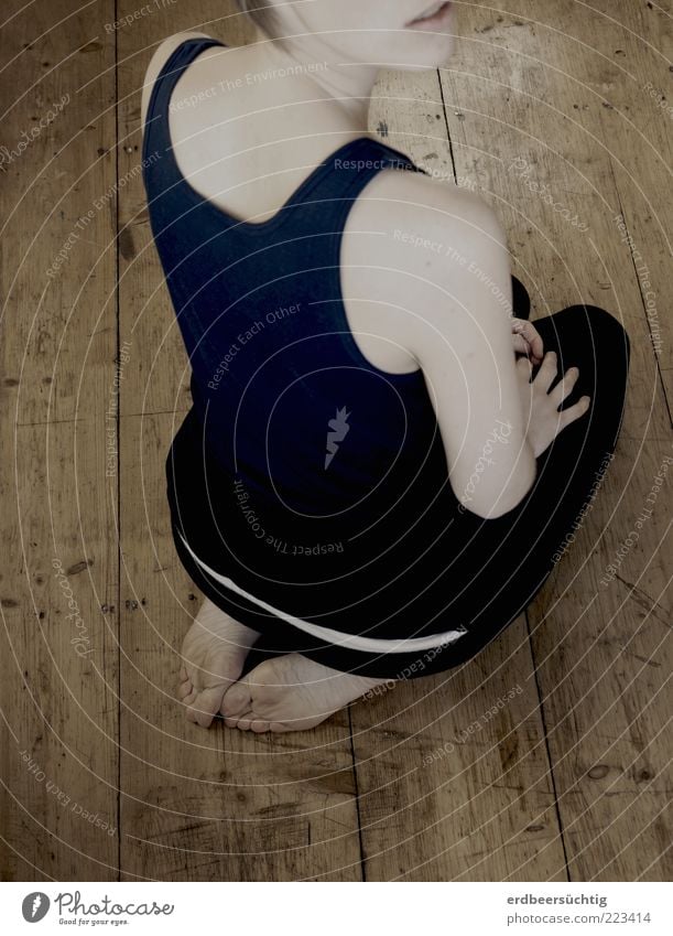 weibliche Person hockt mit Rücken zum Betrachter auf Holzboden; entsättigte Farben. Vom Gesicht nur der Mund angedeutet Yoga Junge Frau Jugendliche Fuß Schulter