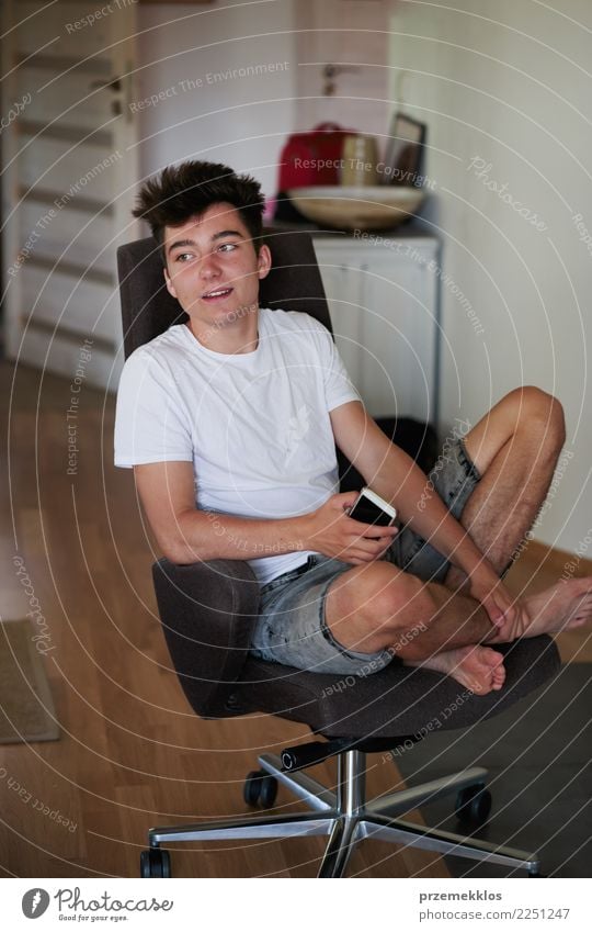 Entspannter Junge mit Smartphone auf einem Stuhl zu Hause Lifestyle Glück Erholung Telefon PDA Technik & Technologie Mensch Junger Mann Jugendliche Erwachsene 1