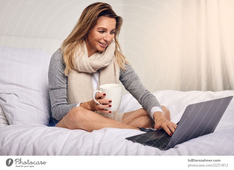 Attraktive Frau, die auf ihrem Bett mit Kaffee sitzt Tee Lifestyle kaufen Glück Zufriedenheit Schlafzimmer Arbeit & Erwerbstätigkeit Computer Notebook