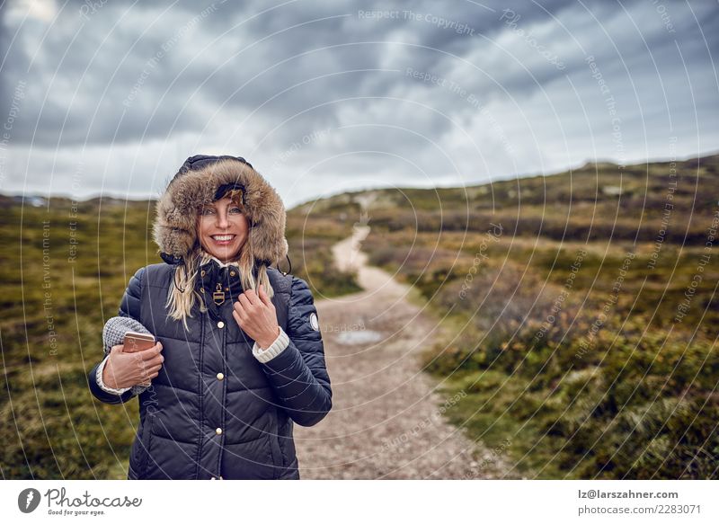Frau von mittlerem Alter, die einem kalten Winter in der Natur trotzt Glück Telefon Handy Erwachsene Landschaft Himmel Unwetter Wind Mantel Lächeln luftig