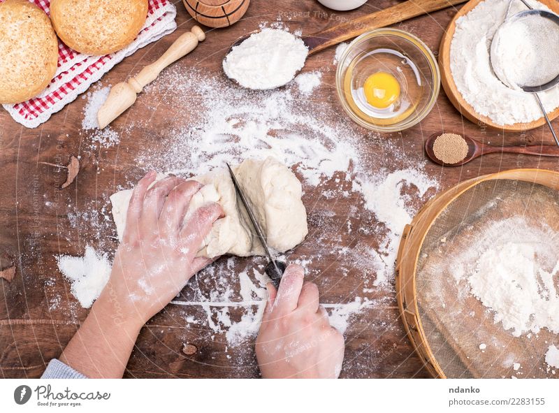 weibliche Hände schneiden mit einem Messer Hefeteig Teigwaren Backwaren Brot Brötchen Schalen & Schüsseln Körper Tisch Küche Frau Erwachsene Arme Hand Sieb Holz