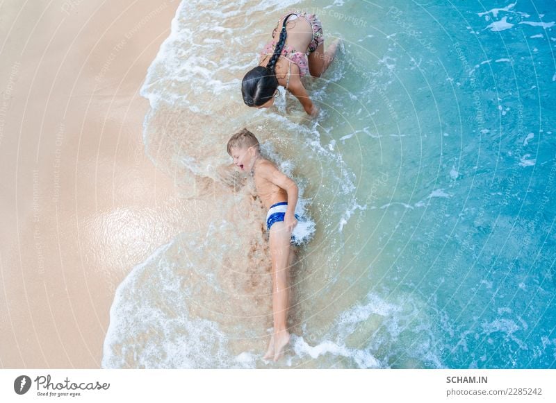 Ein süßer Junge und ein süßes Mädchen haben Spaß am sonnigen tropischen Strand. Auf Sand liegend, wunderbare Wellen um sie herum. Blick von oben Lifestyle