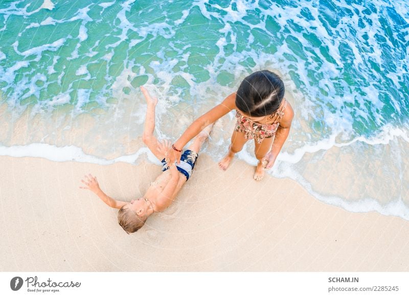Ein süßer Junge und ein süßes Mädchen haben Spaß am sonnigen tropischen Strand. Auf Sand liegend, wunderbare Wellen um sie herum. Blick von oben Lifestyle
