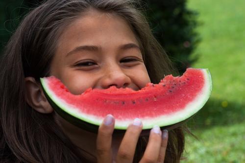 Lächelndes Mädchen mit einer angebissenen Melone vor dem Mund Freude Sommer Garten Kind Kindheit 1 Mensch 8-13 Jahre brünett Essen lachen Fröhlichkeit Glück