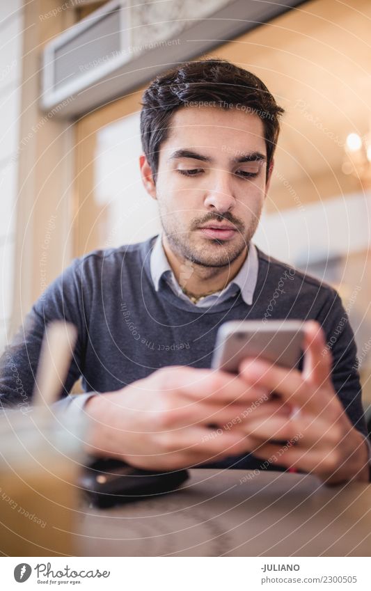 Junger Mann am Café, das sein Telefon betrachtet Frühstück Kaffeetrinken Kommunizieren Lifestyle kaufen Freizeit & Hobby PDA Mensch maskulin Jugendliche