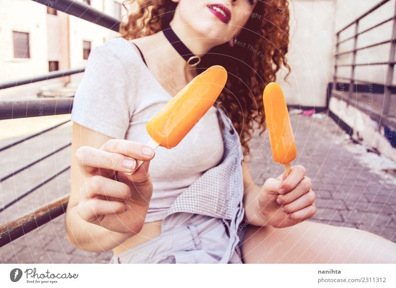 Junge Frau hält zwei orangefarbene Eiscremes in der Hand. Lebensmittel Speiseeis Essen Lifestyle Stil Wellness harmonisch Sommer Sommerurlaub Mensch feminin
