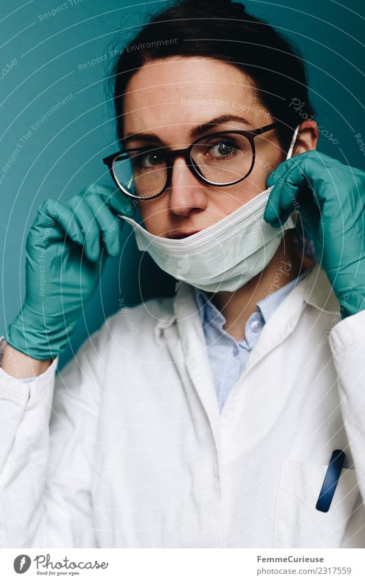 Female doctor putting on her face mask Arbeit & Erwerbstätigkeit Beruf Arzt kompetent anziehen Vorbereitung Brille brünett Kittel Handschuhe türkis