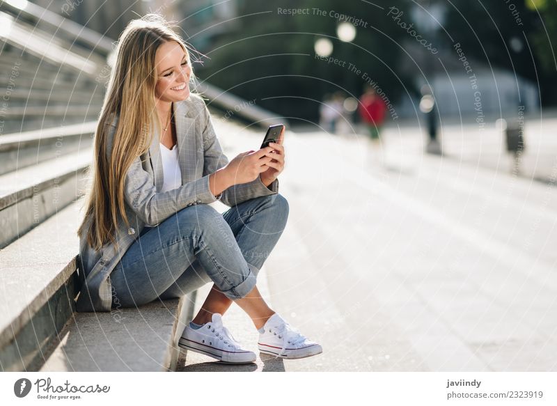 Schöne junge kaukasische Frau schaut auf ihr Smartphone und lächelt im städtischen Hintergrund. Lifestyle Stil Glück schön Haare & Frisuren Telefon PDA Mensch