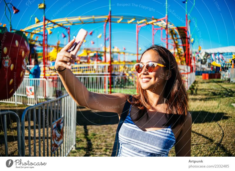 Eine Frau, die einen Selfie in einem Vergnügungspark macht. Farbe mehrfarbig Ausritt PDA Technik & Technologie Sonnenbrille Porträt Jahrmarkt Freude Lächeln