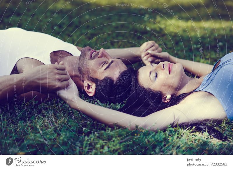 Glücklich lächelndes Paar auf grünem Gras in einem schönen Park liegend Lifestyle Freude Erholung Freizeit & Hobby Mensch Junge Frau Jugendliche Junger Mann