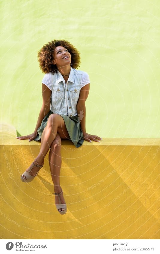 Junge schwarze Frau mit Afrofrisur, die lächelnd an einer Wand sitzt. Lifestyle Stil Glück schön Haare & Frisuren Gesicht Mensch Junge Frau Jugendliche
