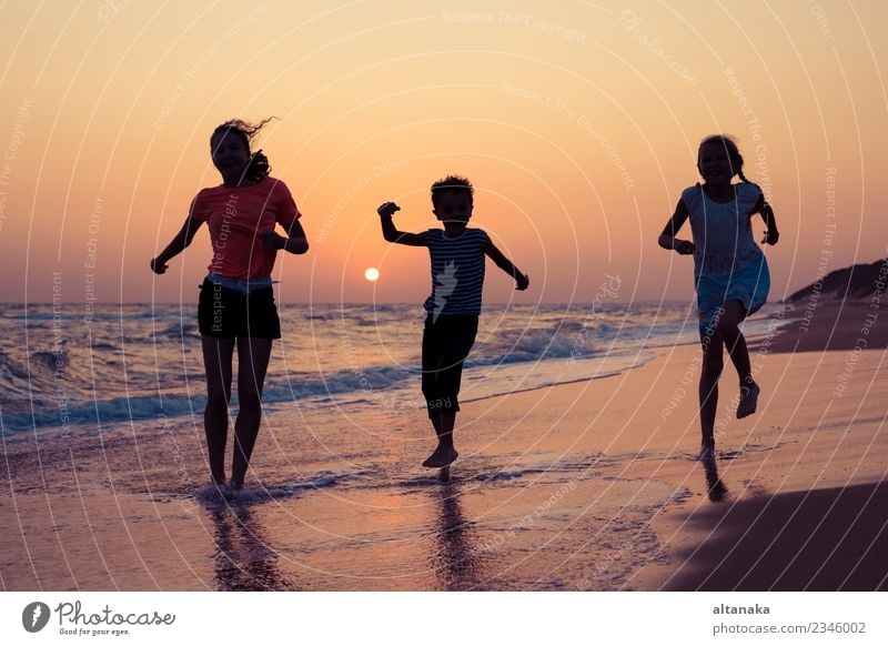 Glückliche Kinder, die zur Zeit des Sonnenuntergangs am Strand spielen. Drei Kinder, die sich im Freien vergnügen. Konzept der Sommerferien und einer freundlichen Familie.