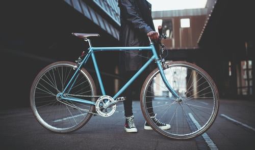 Junger Mann hält blaues Fahrrad in der Stadt. modern Stadtleben Großstadt Schlittschuhlaufen Lifestyle Hipster Schickimicki Mode Bekleidung Jacke erwärmen