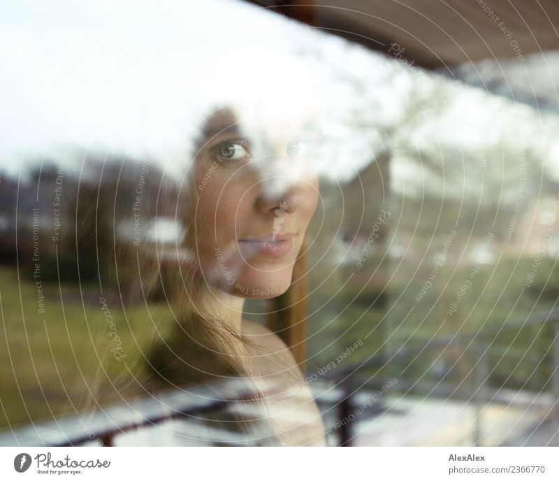 Portrait einer schönen, jungen Frau hinter einer Fensterscheibe mit Reflexionen und Spiegelungen Lifestyle Stil harmonisch Wohnung Balkon Garten Junge Frau