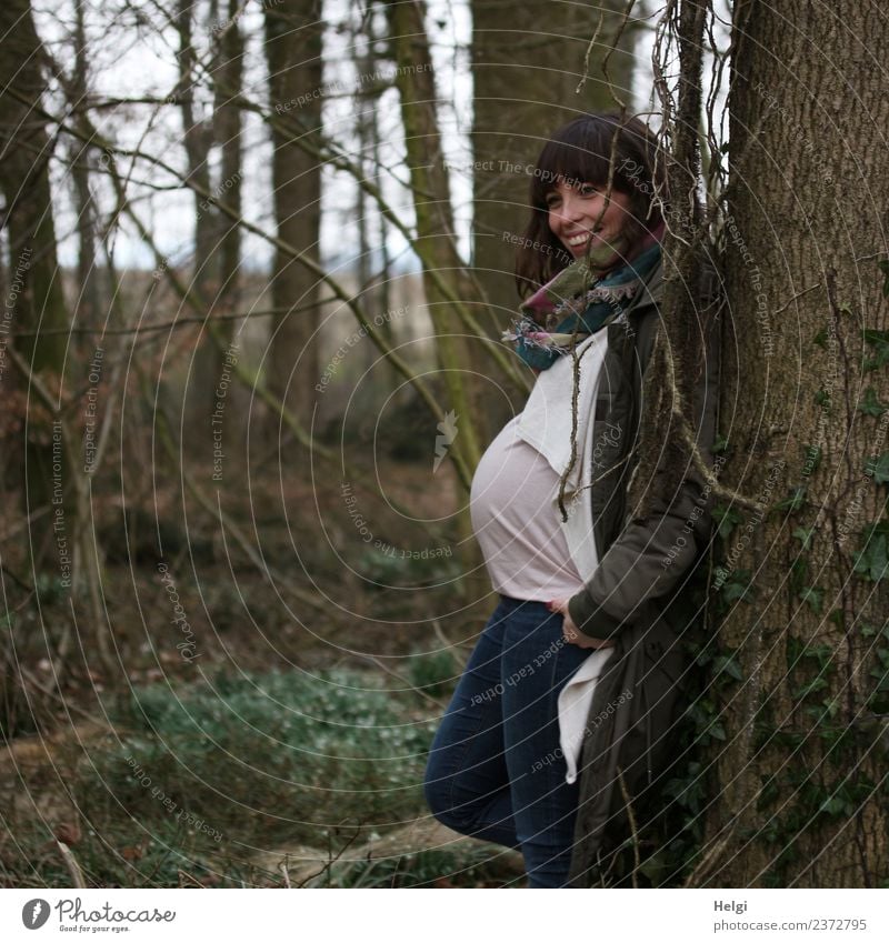 junge schwangere Frau steht lächelnd im Halbprofil an einem Baum Mensch feminin Junge Frau Jugendliche Erwachsene 1 30-45 Jahre Natur Wald Bekleidung T-Shirt
