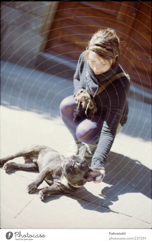 Frau mit Hund. Sonnenbad Mensch Junge Frau Jugendliche 1 Tür Fußgänger Jacke Strumpfhose Haustier Tier braun violett schwarz Farbfoto Außenaufnahme
