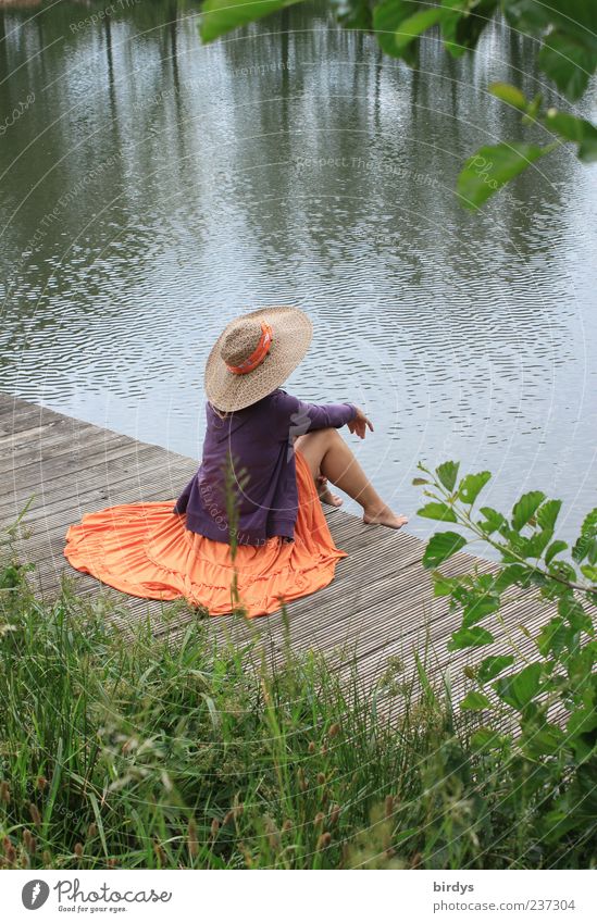 junge barfüßige, verträumte Frau mit Rock und Strohhut sitzt lasziv auf einem Holzsteg am See Junge Frau feminin elegant Strohut Stil Mensch Wasser erotisch