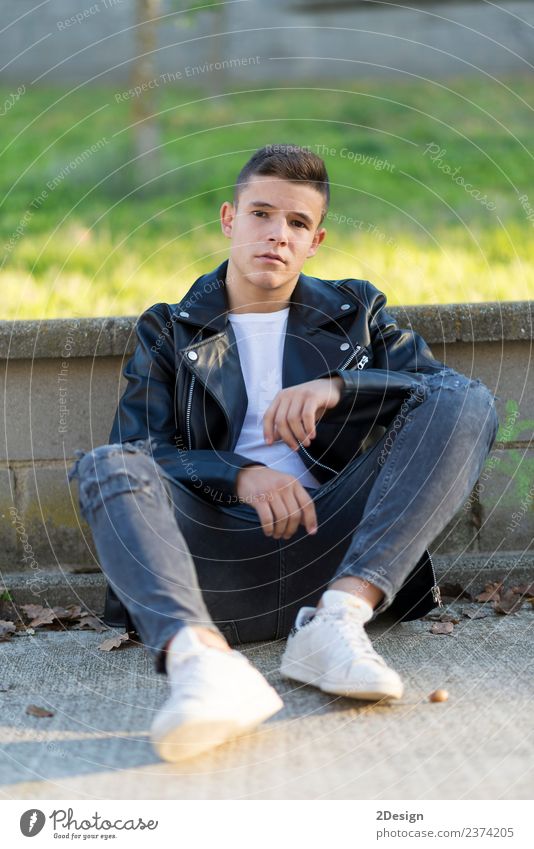 Junger Mann, der im Freien sitzt und eine schwarze Lederjacke trägt. Stil Mensch maskulin Jugendliche Erwachsene 1 13-18 Jahre Mode Bekleidung Jeanshose Jacke