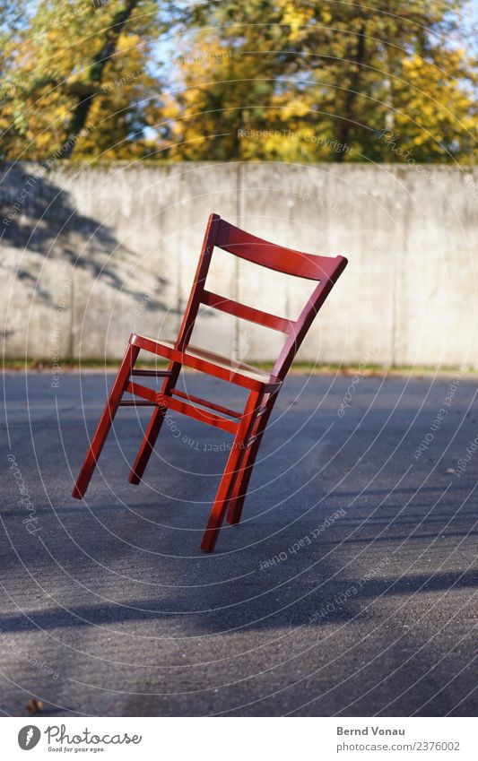 Roter Holz-Stuhl in Schräglage auf sonnigem Asphalt hell mehrfarbig Neigung Gleichgewicht unsicher vierbeinig Vierbeiner klassisch Beton lackiert hotchair