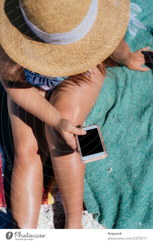 Eine junge Frau, die am Strand schreibt. Jugendliche 18-30 Jahre Junge Frau Beine Hut Decke Handtuch PDA Technik & Technologie Außenaufnahme WiFi Daten Bikini