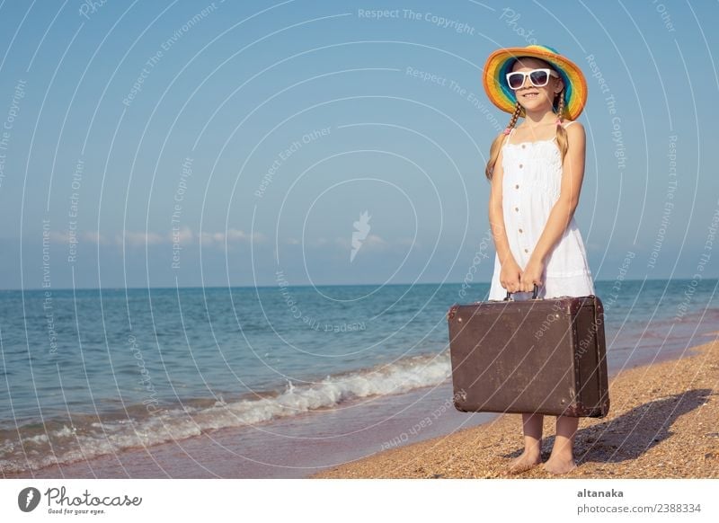 Ein glückliches kleines Mädchen mit Koffer, das am Strand steht. Lifestyle Freude Glück Erholung Freizeit & Hobby Spielen Ferien & Urlaub & Reisen Tourismus