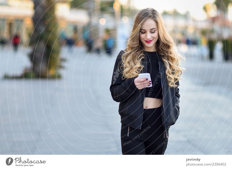Blonde Frau schreibt mit ihrem Smartphone im Freien. Lifestyle Stil schön Haare & Frisuren Telefon PDA Mensch Erwachsene Herbst Straße Mode Jacke blond Lächeln