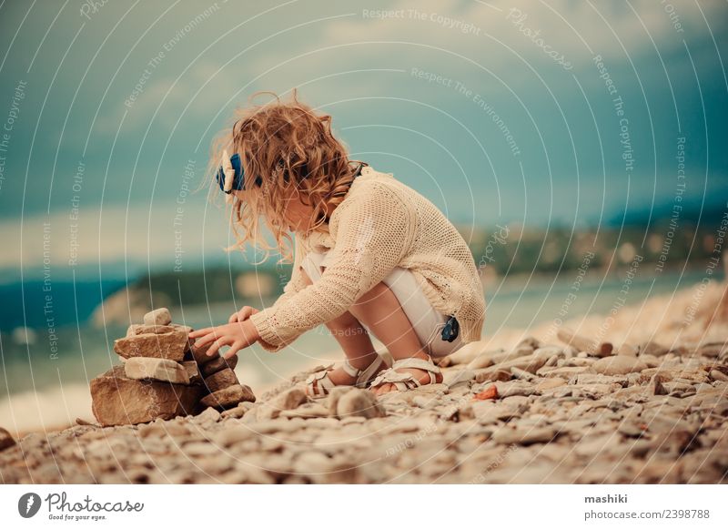 Kind Mädchen spielt mit Steinen am Strand Freude schön Spielen Ferien & Urlaub & Reisen Sommer Meer Himmel Wolken Felsen Fluggerät sitzen klein niedlich blau