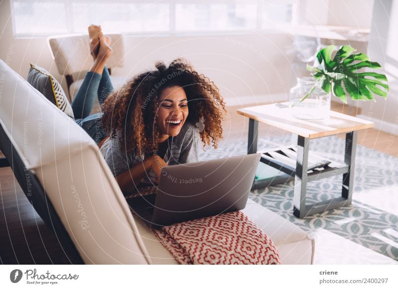 glückliche afrikanische Frau, die auf der Couch liegt und ihren Laptop benutzt. Lifestyle Glück schön Haus Dekoration & Verzierung Sofa