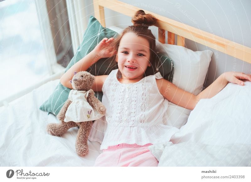 glückliches Kind Mädchen erwacht am frühen Morgen Lifestyle Freude Glück Haare & Frisuren Erholung Sonne Schlafzimmer Spielzeug Teddybär Lächeln schlafen