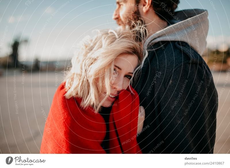 Junge blonde Frau, die in die Kamera schaut, während sie ihren Freund im Freien umarmt. Lifestyle Freude Sonne Winter Erwachsene Mann Paar Mode Lächeln Liebe