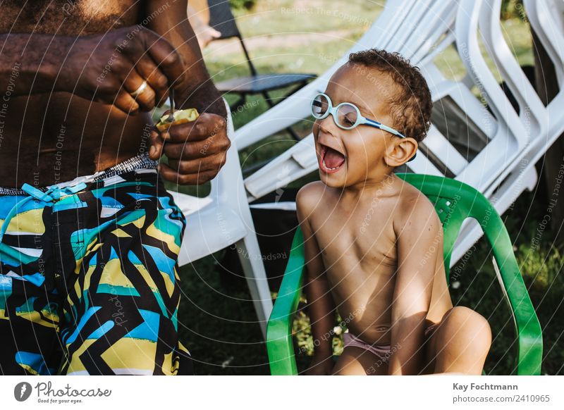 Schwarzer Vater füttert seinen Sohn mit einer Kiwi Frucht Ernährung Essen Löffel Lifestyle Freude Ferien & Urlaub & Reisen Sommer Sommerurlaub Garten Kind Junge