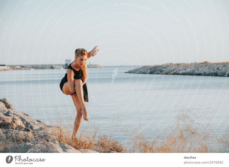 Blonde weiße Frau in schwarzem Kleid führt zeitgenössischen Tanz in der Nähe der Meeresküste. Lifestyle Freude Körper Sport Fitness Sport-Training Mensch