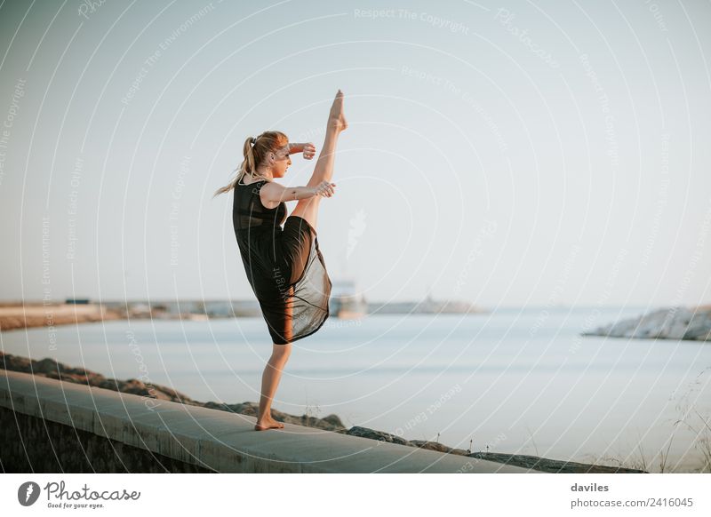 Junge Tänzerin in schwarzem Kleid, die ein Bein hochhebt, im Freien, mit dem Meer im Hintergrund. Lifestyle Freude Körper Ferien & Urlaub & Reisen Tanzen Sport