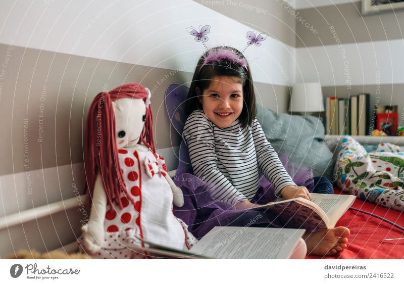 Kleines Mädchen, verkleidet als Schmetterling, sitzt auf dem Bett und liest ein Buch Lifestyle Glück schön Spielen lesen Lampe Schlafzimmer Kind Mensch Frau