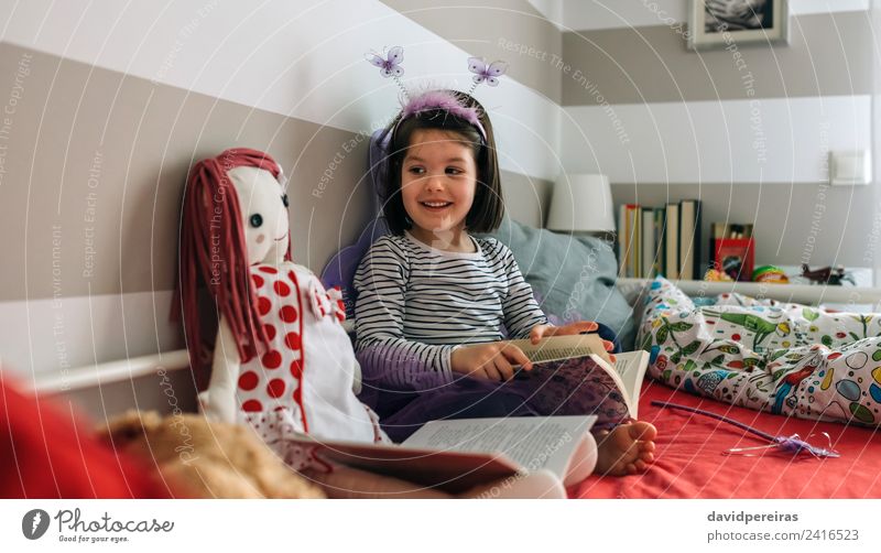Mädchen verkleidet als Schmetterling, liest mit ihrer Puppe. Lifestyle Glück schön Spielen lesen Lampe Schlafzimmer Kind Mensch Frau Erwachsene Freundschaft