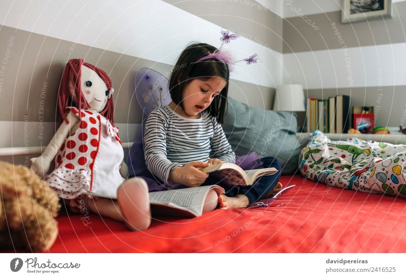 Kleines Mädchen, das verkleidet auf dem Bett sitzt und ein Buch liest Lifestyle schön Spielen lesen Schlafzimmer Kind Schule sprechen Mensch Frau Erwachsene
