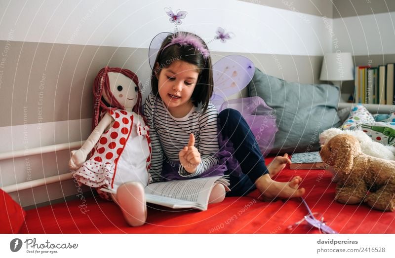 Mädchen verkleidet, die ihrer Puppe ein Buch vorliest. schön Spielen lesen Schlafzimmer Kind sprechen Mensch Frau Erwachsene Freundschaft Schmetterling Flügel
