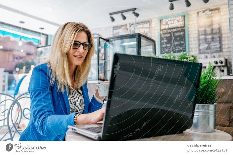 Frau mit Laptop beim Kaffeetrinken lesen Arbeit & Erwerbstätigkeit Arbeitsplatz Computer Notebook Internet Mensch Erwachsene Pflanze blond fahren authentisch
