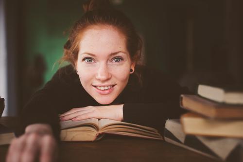 Innenporträt einer rothaarigen glücklichen Frau beim Lernen Lifestyle Erholung lesen Tisch Studium Erwachsene Buch Bibliothek Pullover lernen träumen dunkel
