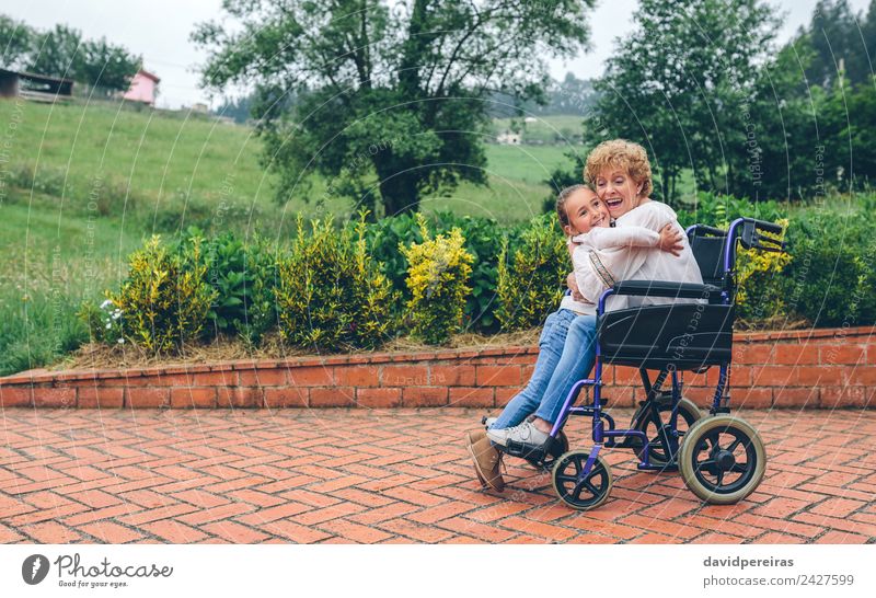 Enkelin umarmt Großmutter im Rollstuhl Lifestyle Glück Gesundheitswesen Erholung Garten Mensch Frau Erwachsene Familie & Verwandtschaft Natur Pflanze Baum Gras