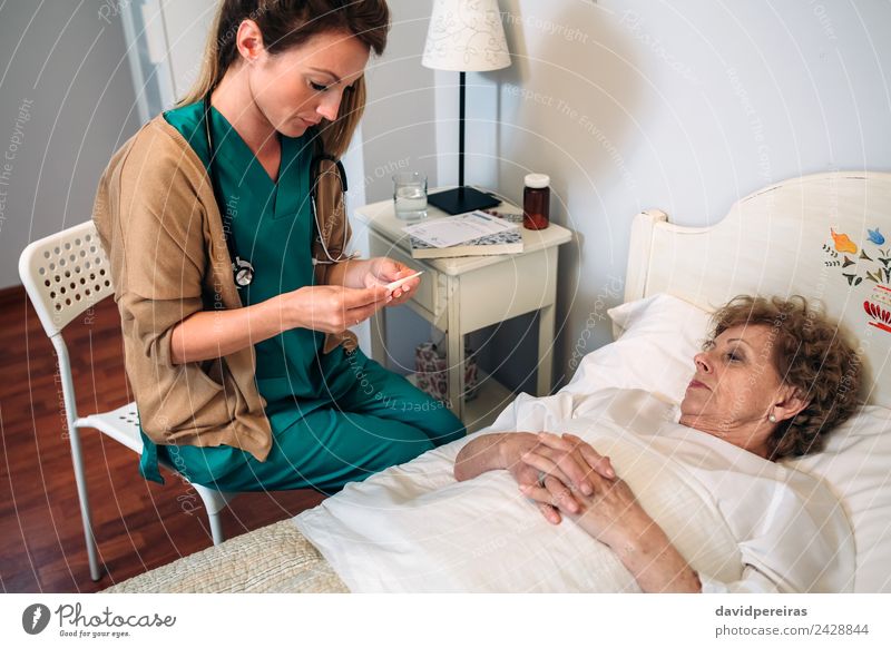 Arzt misst die Temperatur der älteren Frau Gesundheitswesen Krankheit Medikament Haus Stuhl Krankenhaus Mensch Erwachsene alt authentisch Haushaltshilfe