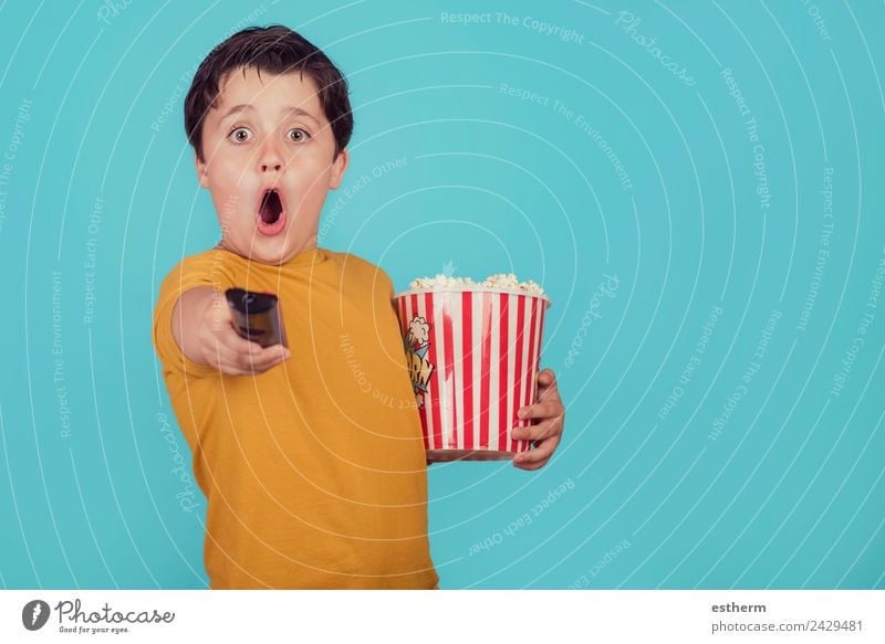 überraschter Junge mit Popcorn und Fernsehfernbedienung auf blauem Hintergrund Lebensmittel Ernährung Fastfood Lifestyle Freude Freizeit & Hobby Mensch maskulin